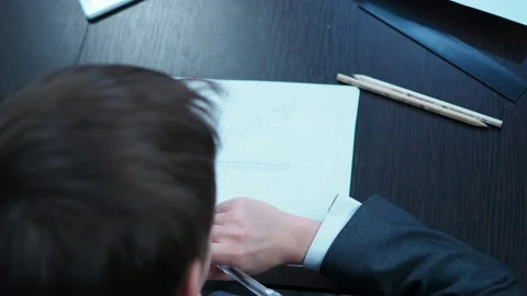 A boy in a jacket draws a graph in a notebook and explains it Stock Footage 144179943