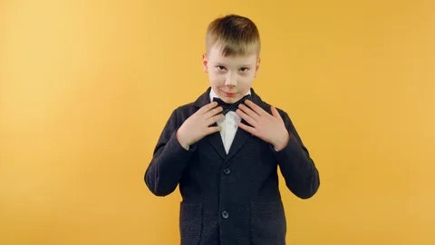 Boy in jacket fixing bow tie looking at camera and smiling on yellow background Video stock 126178629