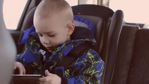 A boy in a jacket sits in a car looking for something on the phone Stock Footage 172537936