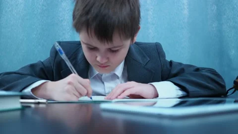 A boy in a jacket writes in a notebook then looks at the frame and smiles Stock Footage 144179855