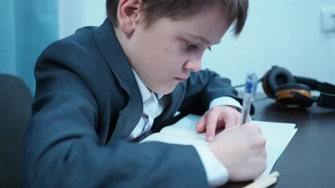 A boy in a jacket writes with a pen in a notebook in a lesson Stock Footage 144179916