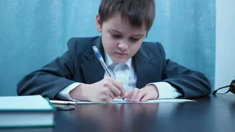 A boy in a jacket is writing in a notebook at the Desk Stock Footage 144179642