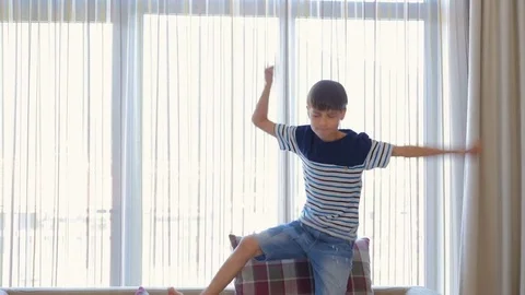 The boy is jumping on the couch. The boy is dancing on the couch.  Stock Footage 77401758
