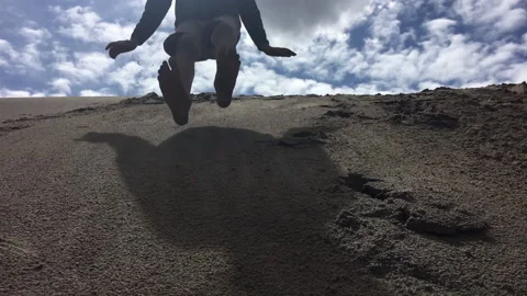 Boy Jumping Off a Sand Dune Toward Camera Stock Footage 130296192