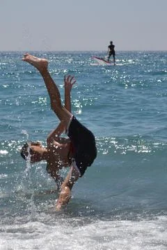 Boy jumping into the sea upside down surrounded by sea foam and in the backgr Stock Photos