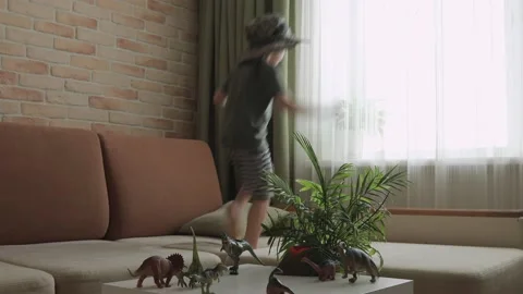 A boy jumping on sofa with dinosaur figurines on the table. The little explor Stock Footage 147673570