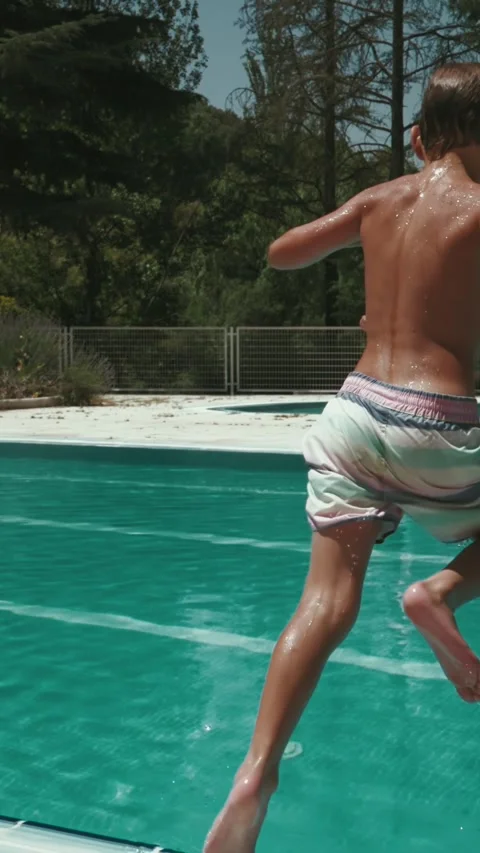 Boy jumping into swimming pool on a hot summer day. Slow motion, vertical video. Stock Footage 313891004