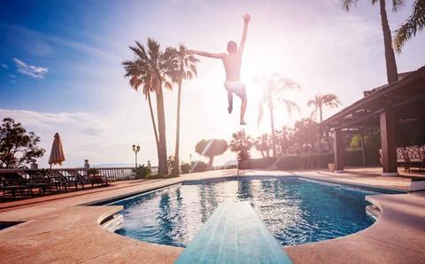 Boy jumps from diving board to pool and lit with sunset light Foto stock