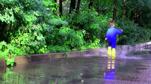 The boy jumps in a puddle . A boy in rubber boots. Happy childhood. Summer Stock Footage 150063968