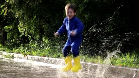 The boy jumps in a puddle . A boy in rubber boots. Happy childhood. Summer Stock Footage 150064022