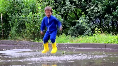 The boy jumps in a puddle . A boy in rubber boots. Happy childhood. Summer Stock Footage 150064071