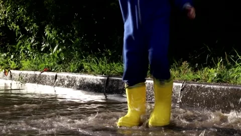 The boy jumps in a puddle . A boy in rubber boots. Happy childhood. Summer Stock Footage 150064197