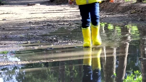 The boy jumps in a puddle . A boy in rubber boots. Happy childhood. Summer Stock Footage 150064275