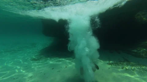 Boy jumps from a rock into the sea, captured in an immersive over-under shot Stock Footage 313809236