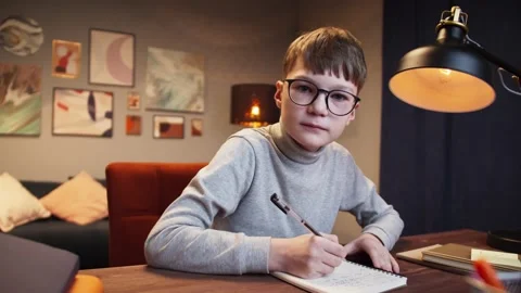 Boy kid in glasses making video call with laptop at home, writing notes, using Stock Footage 153091101