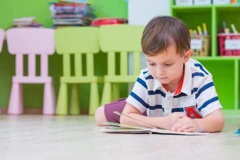 Boy kid lay down on floor and reading tale book  in preschool library,Kinderg Foto stock