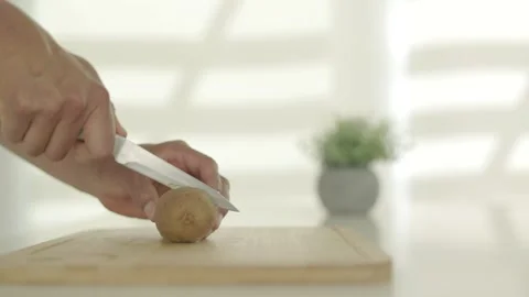 Boy in the kitchen cutting a kiwi to prepare a fruit smoothie after training. Video stock 244733345