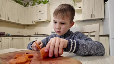 Boy in kitchen preparing food, cutting boiled carrots for salad Stock Footage 303494815
