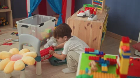 Boy kneeling and opening red toy case with hands beside blocks and plush, f.. Stock Footage 339248398