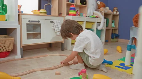 Boy kneeling, hands assembling wooden train track and toy car on floor in a.. Stock Footage 339205646