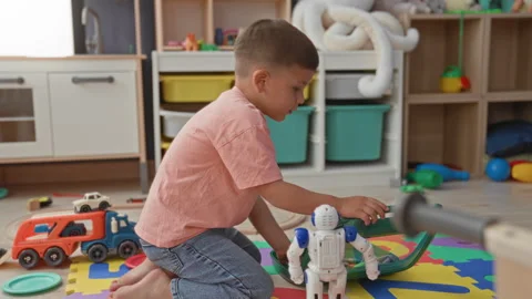 Boy kneeling on playmat touching robot toy with hand among train tracks and.. Stock Footage 339161463