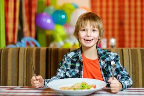 Boy with knife and fork in front of salad. Teenager eating at cafe Stock Photos