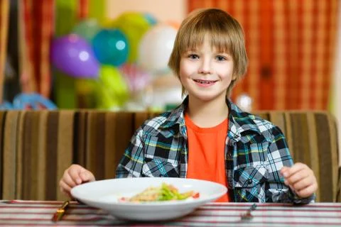 Boy with knife and fork in front of salad. Teenager eating at cafe Stock Photos