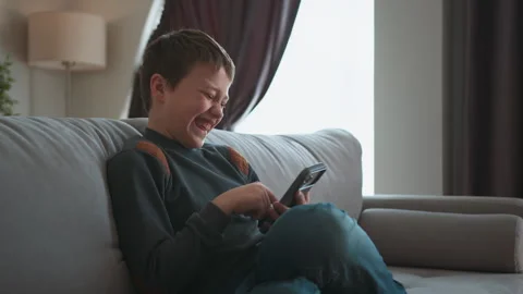 Boy Laughing While Using Phone. Joyful child digital amusement cozy home Stock Footage 335480151