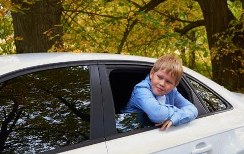 Boy leaned out of the window of a parked white car Stock Photos