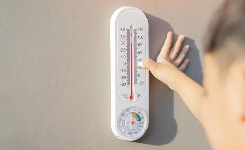 The boy learn to checking the numbers on a thermometer on a gray wall outsi.. Foto stock