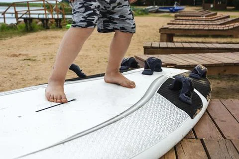 Boy learn to stand on the surf on the beach on the shore of the lake, sea, wa Stock Photos