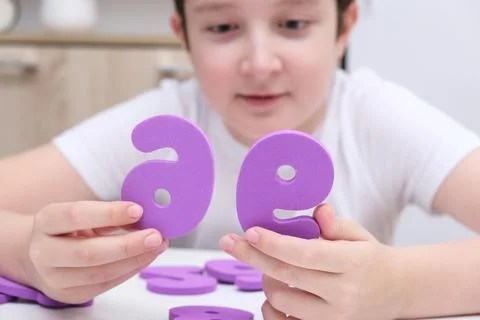 A boy learning math, count exercises at home, holding colorful foam numbers in Stock Photos