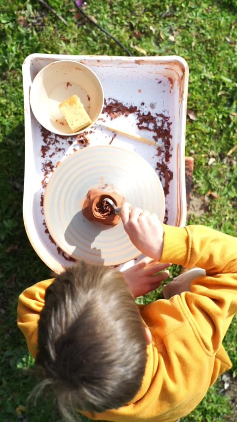 Boy learning to use potter's wheel outdoors Stock Footage 263757459