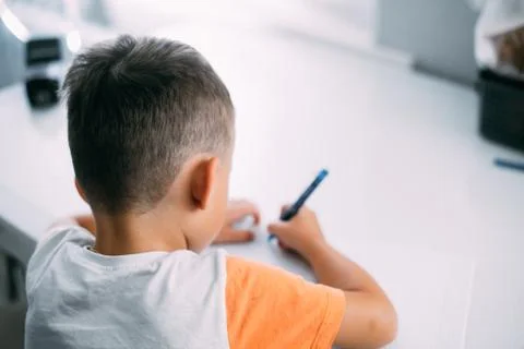 A boy is learning to write the letter K in a notebook preparing for school Stock Photos