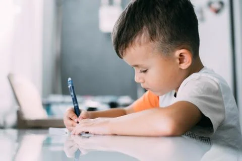 A boy is learning to write the letter K in a notebook preparing for school Foto stock