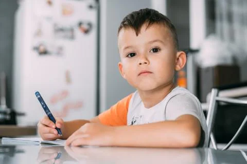 A boy is learning to write the letter K in a notebook preparing for school Stock Photos