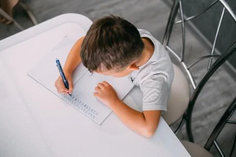A boy is learning to write the letter K in a notebook preparing for school Stock Photos