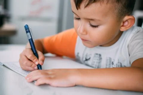 A boy is learning to write the letter K in a notebook preparing for school Stock Photos