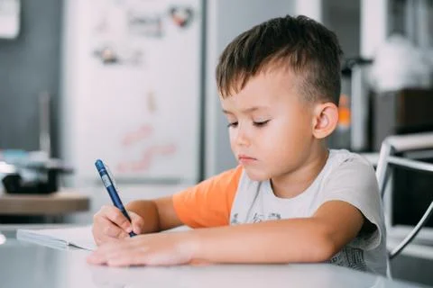 A boy is learning to write the letter K in a notebook preparing for school Stock Photos
