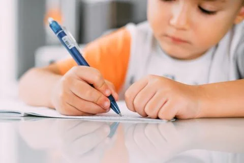 A boy is learning to write the letter K in a notebook preparing for school Stock Photos