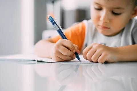 A boy is learning to write the letter K in a notebook preparing for school Stock Photos