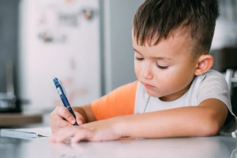 A boy is learning to write the letter K in a notebook preparing for school Stock Photos