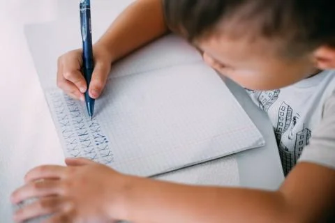 A boy is learning to write the letter K in a notebook preparing for school Stock Photos