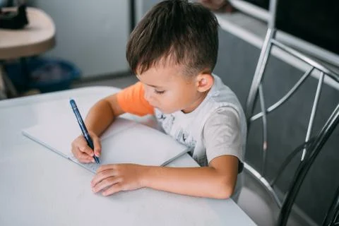 A boy is learning to write the letter K in a notebook preparing for school Stock Photos