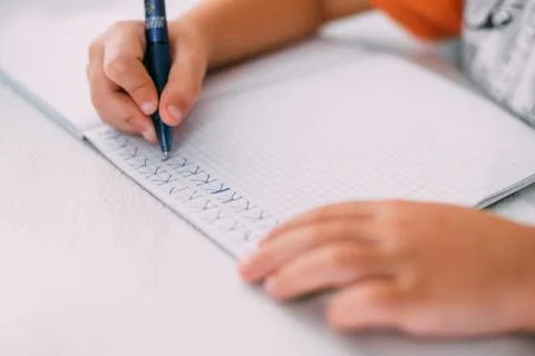 A boy is learning to write the letter K in a notebook preparing for school Stock Photos