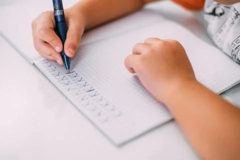 A boy is learning to write the letter K in a notebook preparing for school Stock Photos