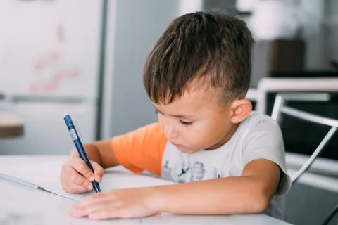A boy is learning to write the letter K in a notebook preparing for school Stock Photos