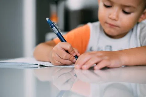 A boy is learning to write the letter K in a notebook preparing for school Stock Photos