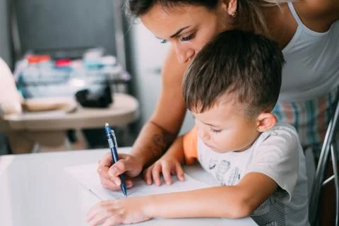 A boy is learning to write the letter K in a notebook preparing for school Stock Photos