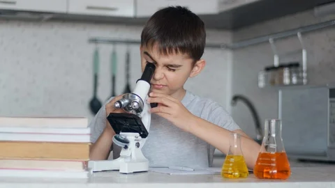 A boy learns chemistry using a microscope and makes notes in a notebook Stock Footage 127941871